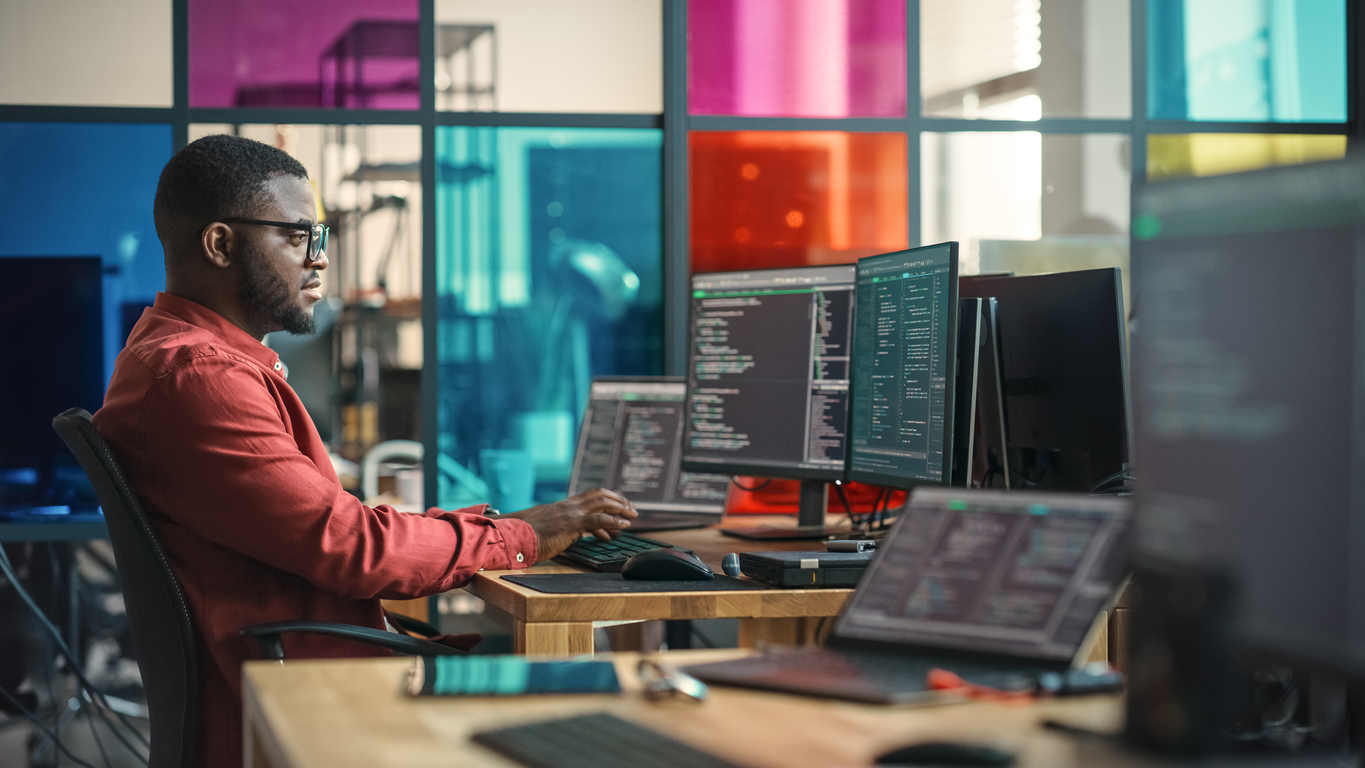 A cybersecurity professional works at a desk with several monitors. 