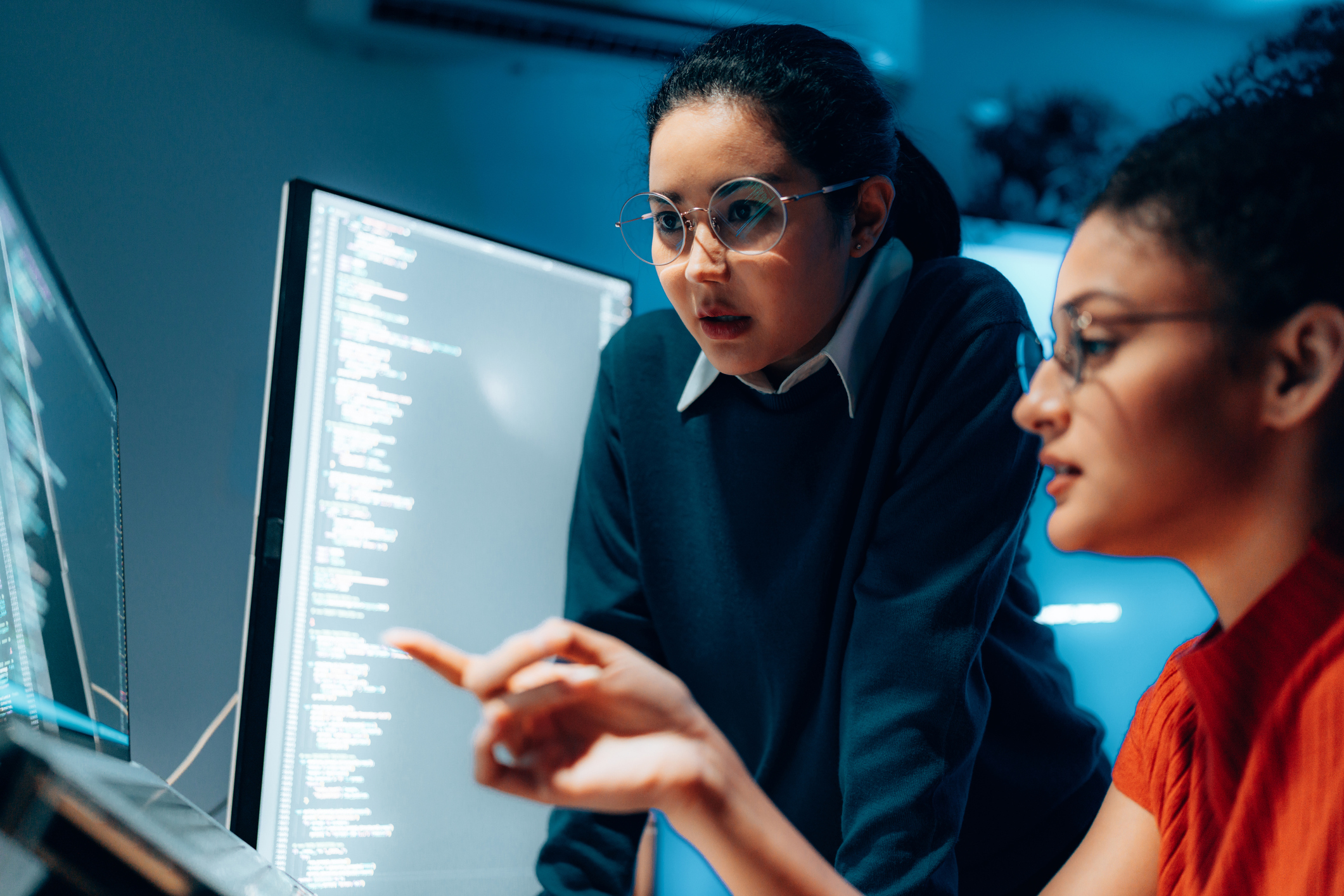 Two cybersecurity professionals review code on a monitor.