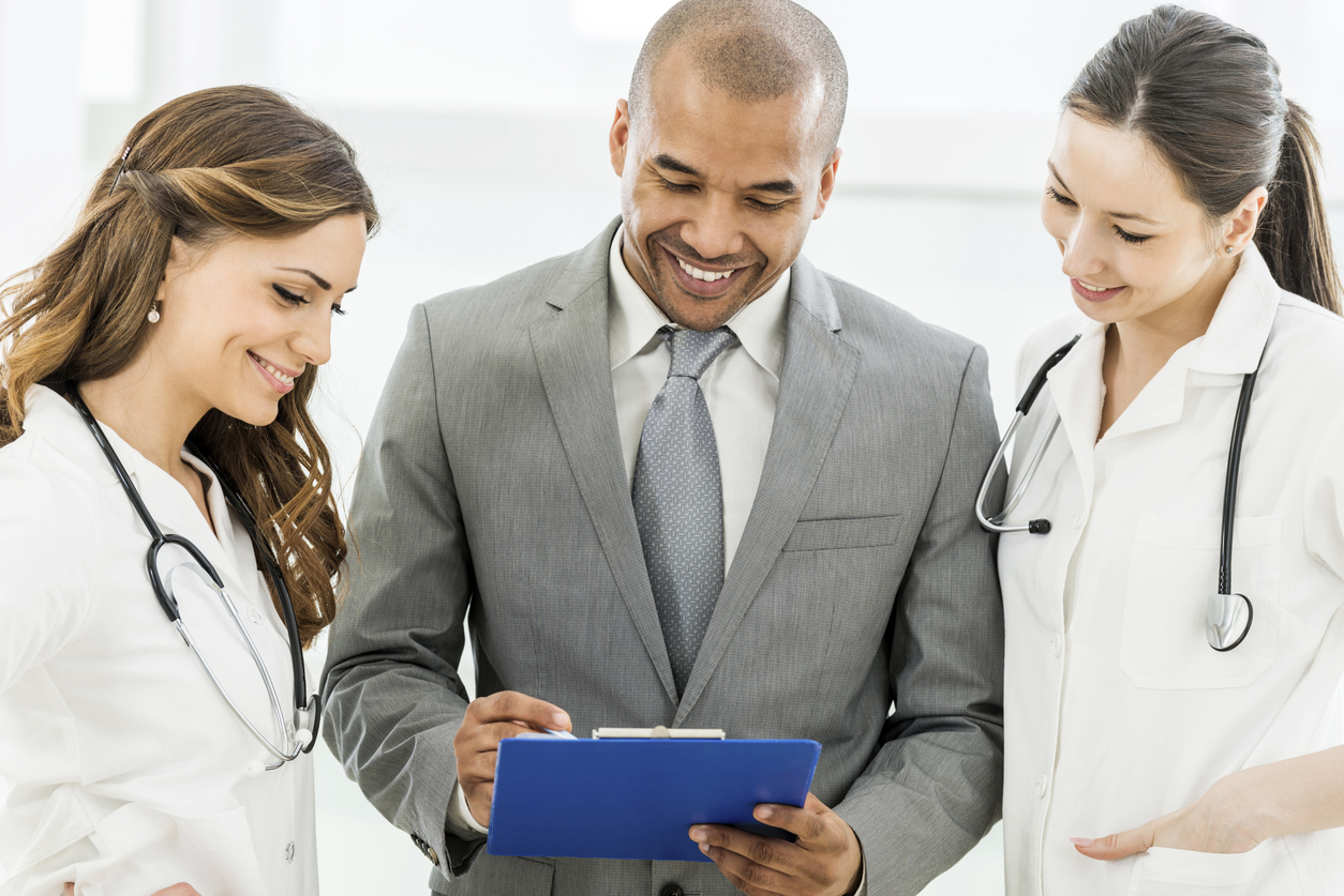 A hospital administrator shows two clinicians a document on a clipboard.