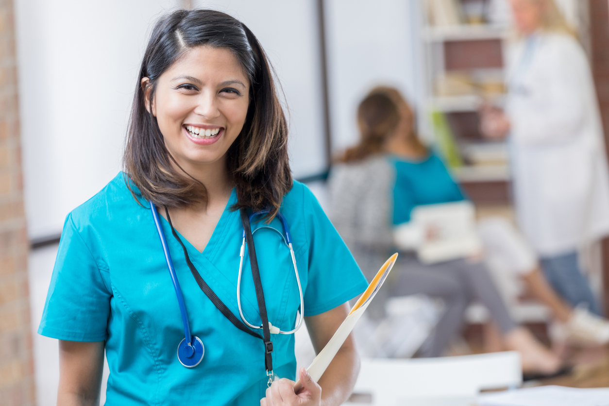 A smiling nurse in scrubs holding a patient’s file.