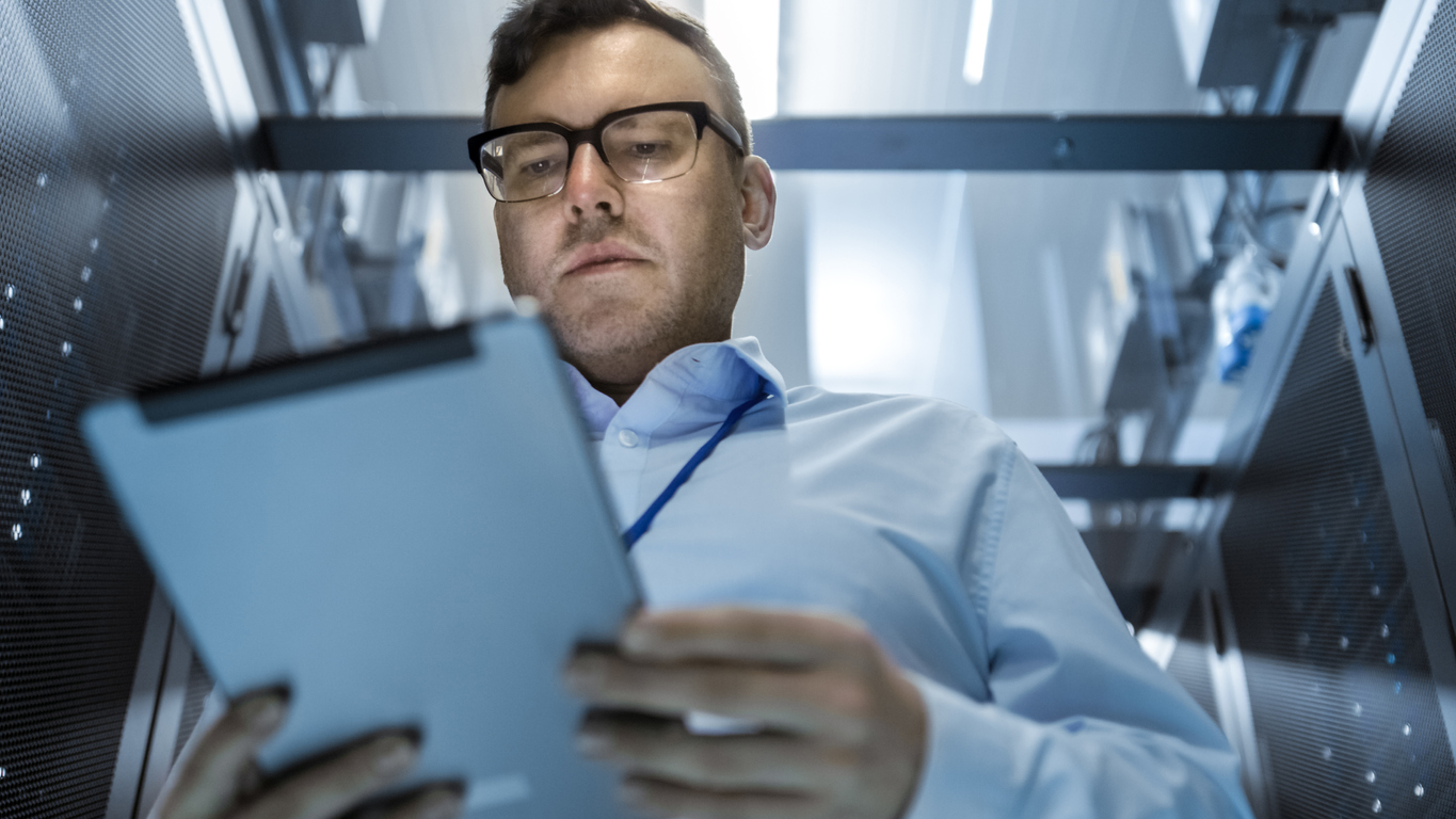 A cybersecurity professional in a server room consults a tablet.