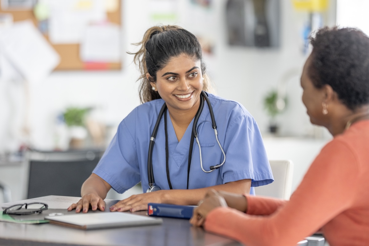 A nurse in scrubs smiles at a patient.