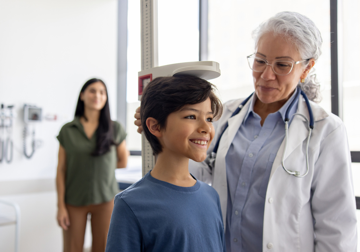 A family nurse practitioner in a white coat measures the height of a child patient. 