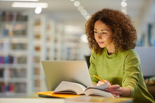 A nursing student works on their DNP project on a laptop in a library.