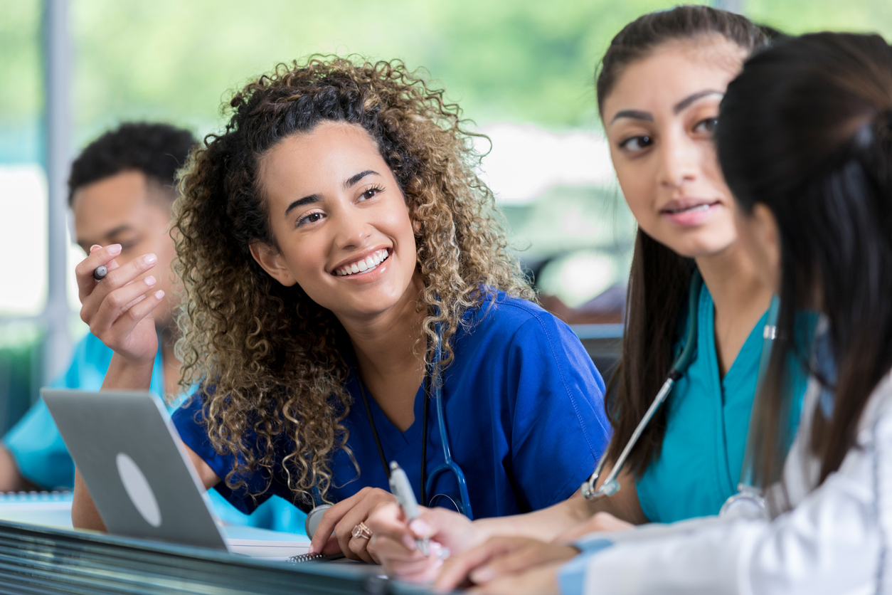 Nursing students in scrubs studying together with a laptop and notebooks.