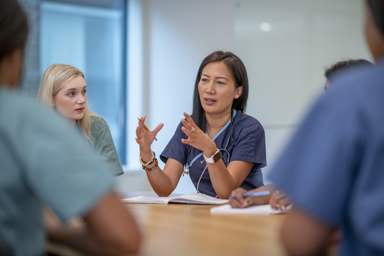 A nurse in scrubs talking to colleagues at a conference table. 